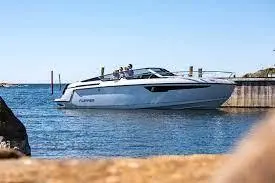 A sleek motorboat with two people docked at a marina against a clear blue sky and calm water.